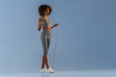 Spor kıyafetli bir kadın atlama ipini stüdyo arka planında tutuyor. En iyi kardiyo çalışması