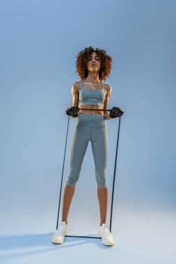 Woman performs exercises with expander on studio background. Strength and motivation