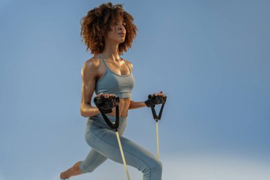 Woman performs exercises with expander on studio background. Strength and motivation