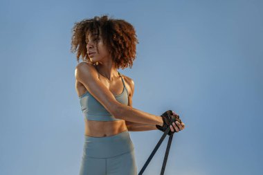 Woman performs exercises with expander on studio background. Strength and motivation