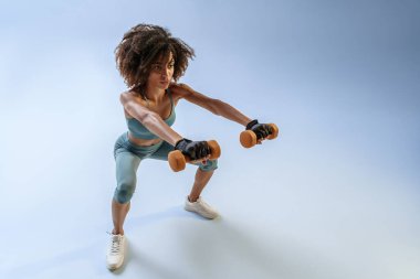 Stüdyo arka planında dambıllarla egzersiz yapan bir kadın. Spor ve sağlıklı yaşam tarzı