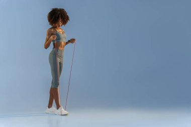 Spor kıyafetli bir kadın atlama ipini stüdyo arka planında tutuyor. En iyi kardiyo çalışması