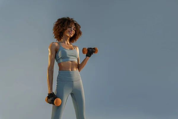 stock image Smiling Muscular woman doing exercise with weight dumbbells on studio background 