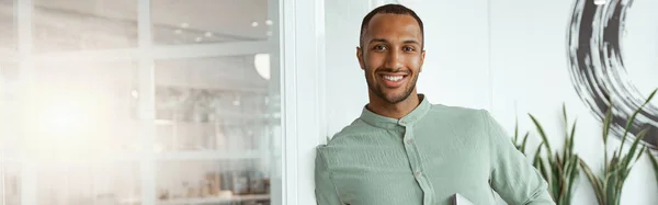 居心地の良いオフィスに立っている間にラップトップを保持しているアフリカのビジネスマンの笑顔 事業概念 — ストック写真