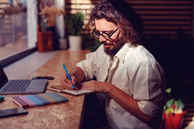 Erkek hippi, pencerenin yanında rahat bir şekilde otururken notlar alıyor. Yüksek kalite fotoğraf