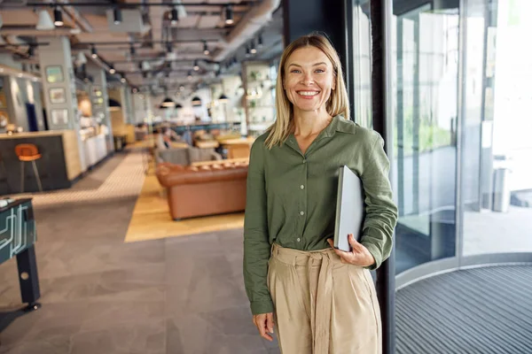 stock image Woman manager in casual clothes standing with laptop in cozy coworking and looking at camera 