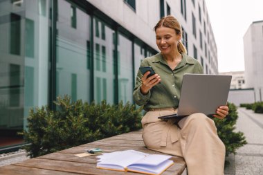 İş kadını ofis dışında bilgisayarını ve telefonunu kullanıyor. Mesafe çalışma kavramı