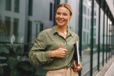 Gülümseyen kadın ofis çalışanı modern binanın arka planında duruyor ve kameraya bakıyor.