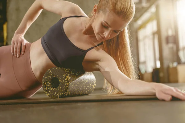 健身妇女在健身房的健身垫上使用泡沫滚筒进行伸展运动和按摩肌肉 — 图库照片