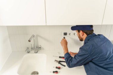 Profesyonel elektrikçi ev mutfağına yeni elektrik soketi yerleştirirken tornavida kullanıyor. 