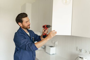 Üniformalı bir erkek işçi mutfak dolabının kapısını tornavidayla tamir ediyor. Ev yenileme konsepti