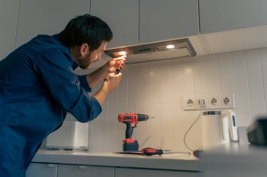Mutfakta modern fırın kaputunu tamir eden üniformalı profesyonel bir erkek işçi. Yüksek kalite fotoğraf
