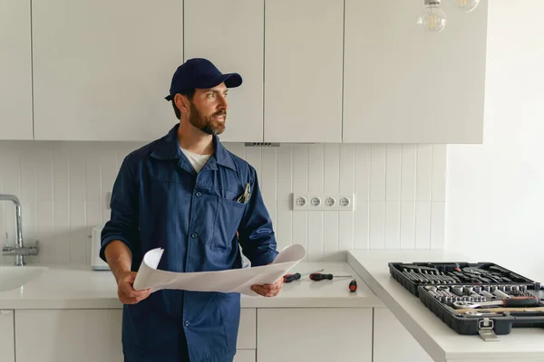 Male worker in uniform standing on kitchen with home plan before starting work. High quality photo