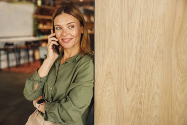 Gülümseyen iş kadınına yakın plan, müşteriyle kafede dururken telefonla konuşmak.