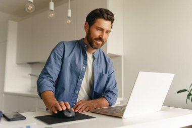 Ev mutfağında dizüstü bilgisayarda çalışan serbest çalışan bir erkek. Mesafe çalışma konsepti. Yüksek kalite fotoğraf