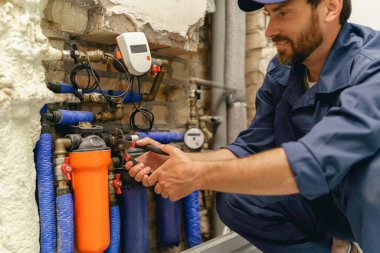 Üniformalı tamirci evde su tedarik sistemini tamir ederken ayarlanabilir İngiliz anahtarı kullanıyor.