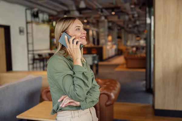 一个微笑的女商人站在咖啡店的时候 正在和客户通电话 — 图库照片