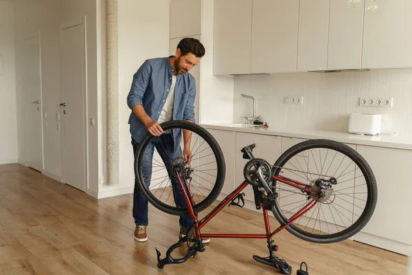 Handsome smiling man in casual clothing repairing bicycle itself at home. High quality photo