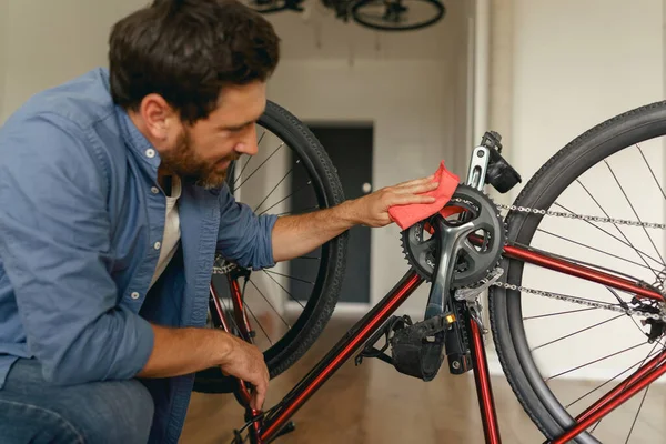 캐주얼 잘생긴 남자는 집에서 먼지로부터 자전거를 청소합니다 품질의 — 스톡 사진