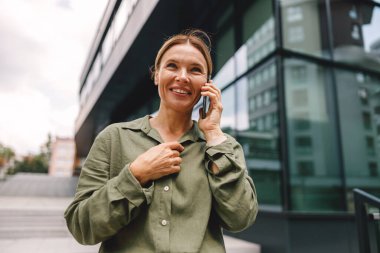Modern binanın arka planında dikilirken telefonla konuşan şık kadın girişimci. 