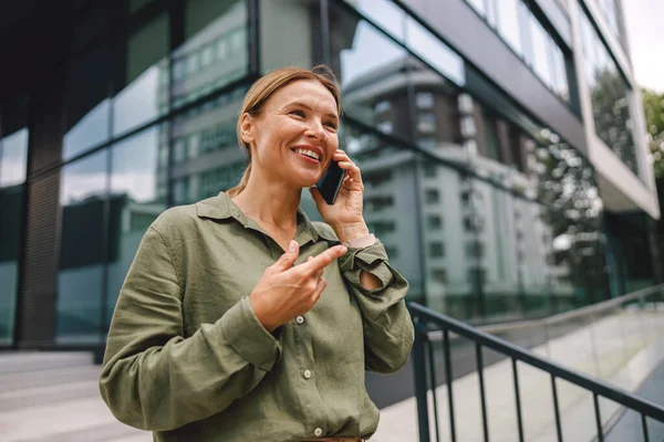 Modern binanın arka planında dikilirken telefonla konuşan şık kadın girişimci. 