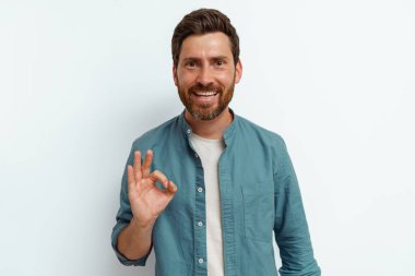 Gülümseyen adam beyaz arka planda duruyor ve parmaklarıyla işaret veriyor. Yüksek kalite fotoğraf
