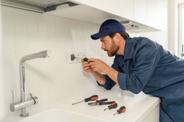 Profesyonel elektrikçi ev mutfağına yeni elektrik soketi yerleştirirken tornavida kullanıyor. 
