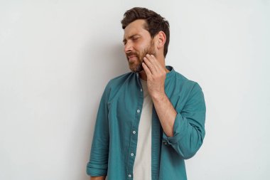 Yakışıklı bir adam beyaz arka planda dururken sakalını kaşır. Yüksek kalite fotoğraf