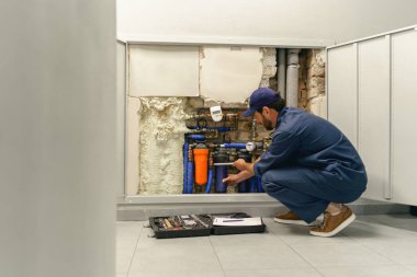 Üniformalı tamirci evde su tedarik sistemini tamir ederken ayarlanabilir İngiliz anahtarı kullanıyor.