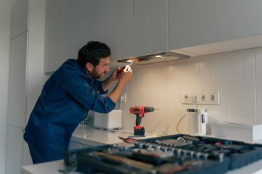 Mutfakta modern fırın kaputunu tamir eden üniformalı profesyonel bir erkek işçi. Yüksek kalite fotoğraf