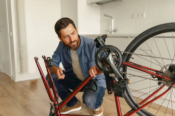 Bonito Homem Sorridente Roupas Casuais Reparando Própria Bicicleta Casa Foto — Fotografia de Stock
