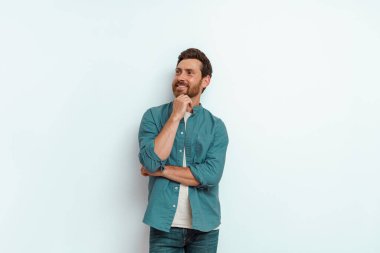 Adam elini çenesinden tutar ve beyaz arka planda düşünceli bir şekilde yana bakar. Yüksek kalite fotoğraf