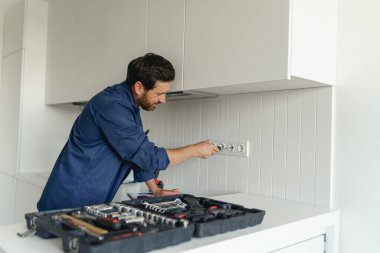 Üniformalı tamirci ev mutfağının elektrik prizini tamir ediyor.