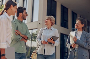 Mola sırasında modern ofis binasının arka planında duran bir grup iş adamı konuşuyor