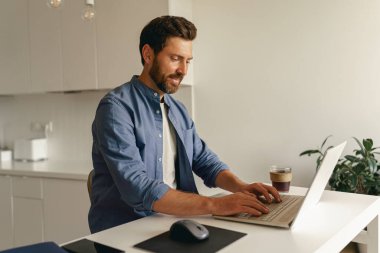 Dizüstü bilgisayarda çalışan ve ev mutfağında kahve içen serbest çalışan bir erkek. Yüksek kalite fotoğraf