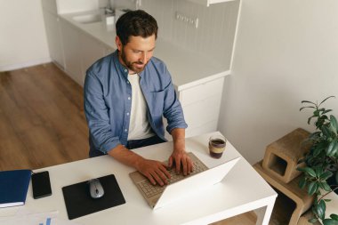 Ev mutfağında dizüstü bilgisayarda çalışan serbest çalışan bir erkek. Mesafe çalışma konsepti. Yüksek kalite fotoğraf