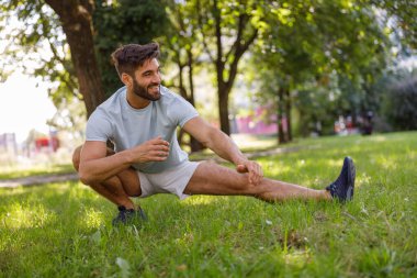 Spor kıyafetli gülümseyen adam şehir parkında koşmadan önce ısınıyor. Yüksek kalite fotoğraf
