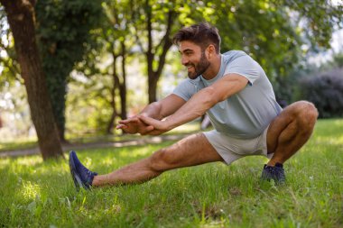 Spor kıyafetli gülümseyen adam şehir parkında koşmadan önce ısınıyor. Yüksek kalite fotoğraf