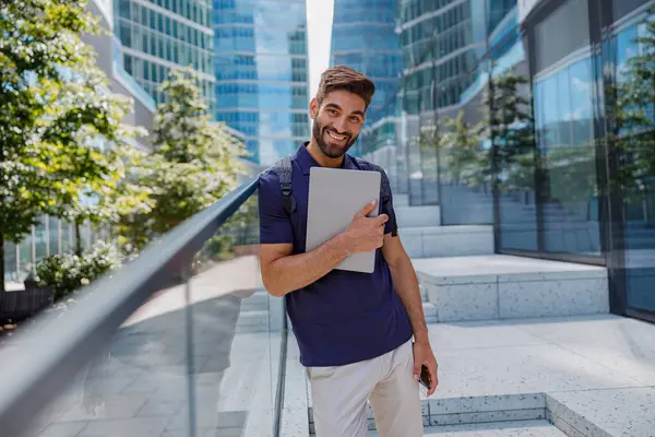 一个英俊的商人站在城市摩天大楼的背景上 带着笔记本电脑 高质量的照片 — 图库照片