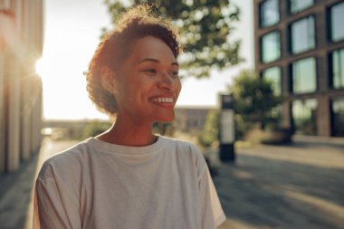 Modern bina arka planında duran güzel, gülümseyen genç bir kadın ve başka tarafa bakıyor. Yüksek kalite fotoğraf