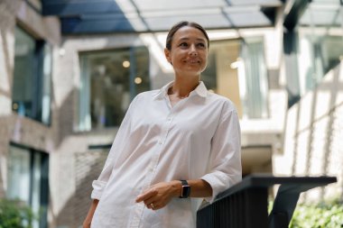 Gülümseyen kadın yöneticinin portresi modern çalışma arka planında duruyor ve başka yere bakıyor.