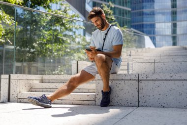 Yakışıklı adam gökdelenlerin arkasında oturuyor ve kulaklıkla müzik dinliyor. Yüksek kalite fotoğraf