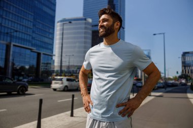 Yakışıklı, spor elbiseli, gülümseyen gökdelenlerin arkasında duran adam.