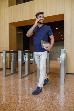 Erkek müdür, ofisin girişinde dizüstü bilgisayarla telefonla konuşuyor ve başka yere bakıyor.