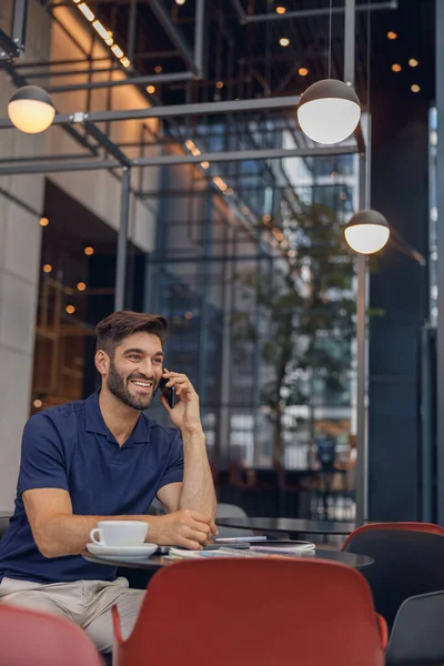 Smiling businessman talking by phone with client sitting in cozy cafe. High quality photo