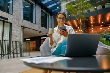 Mola sırasında ofis salonunda kahve içen ve telefonla konuşan kadın müdür.