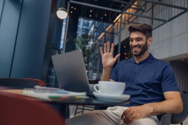 İş adamının iş arkadaşıyla görüntülü görüşmesi ve el sallaması var.
