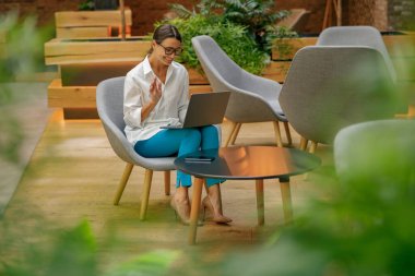 Müşteri ile video görüşmesi yapan ve el sallayan serbest çalışan bir kadın.