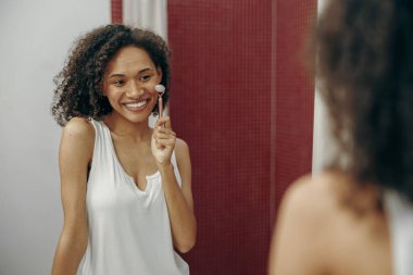 Güzel bir kadın banyoda dikilirken yüzüne masaj yapmak için yeşim taşı kullanıyor. Güzellik merkezi prosedürü