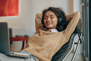 Kulaklıklı gülümseyen kadın molada evde laptopta müzik dinliyor.